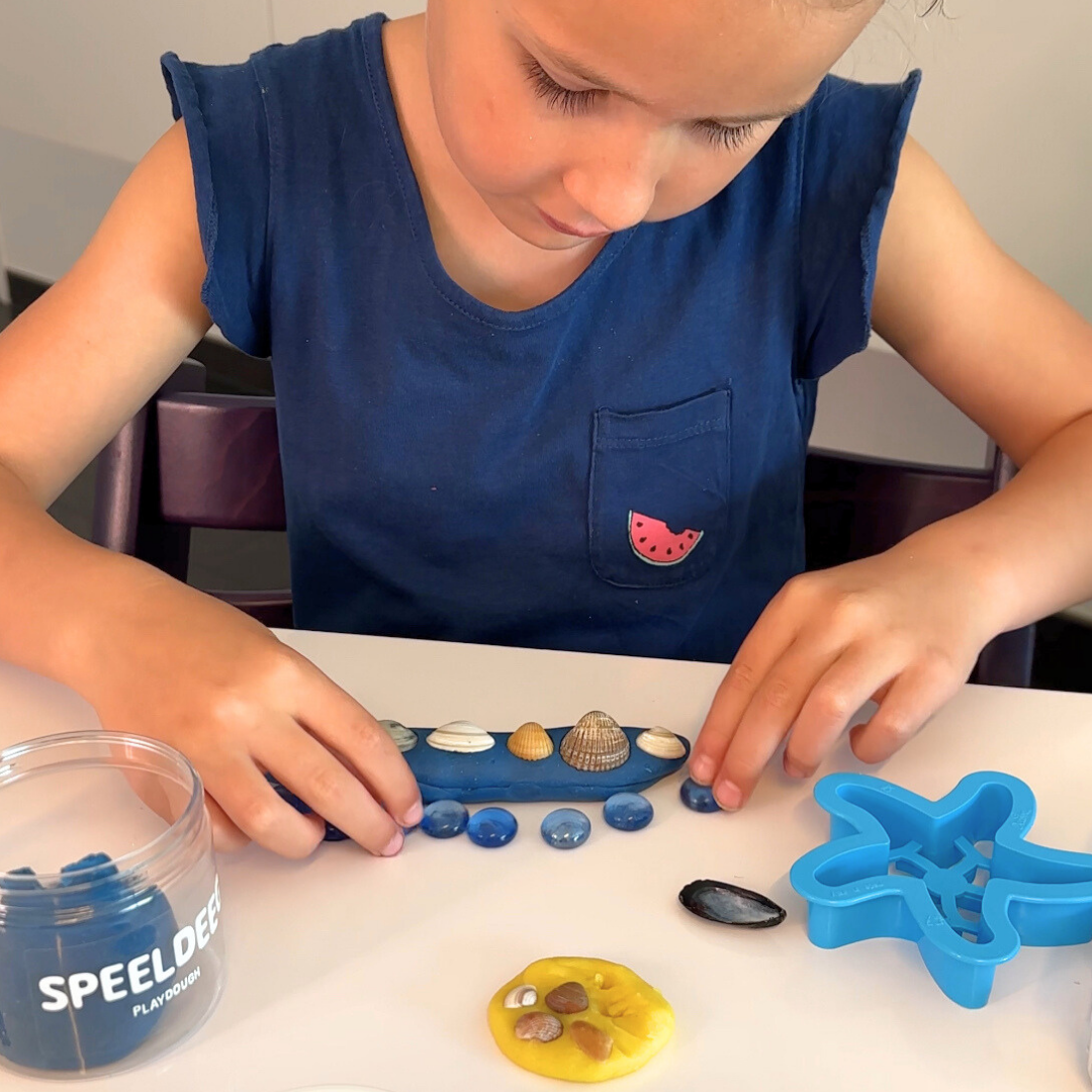 Kind speelt met speeldeeg in zomerthema. Ze maakt afdrukken en kunstwerken met schelpen. 